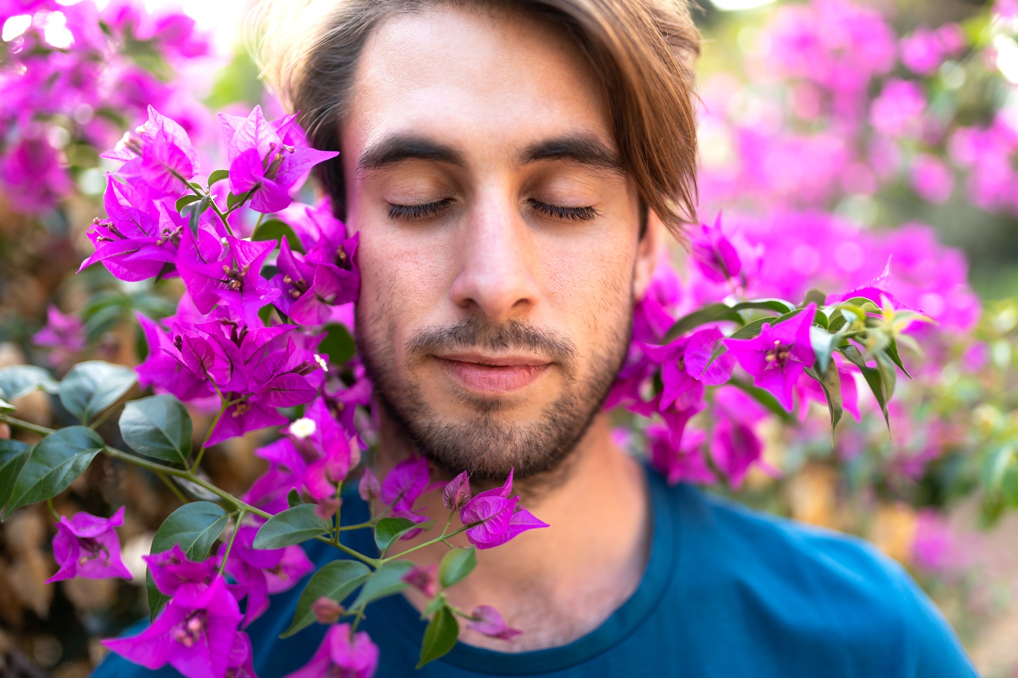 Portrait of young man with closed eyes surrounded by colourful flowers. Connecting with nature.