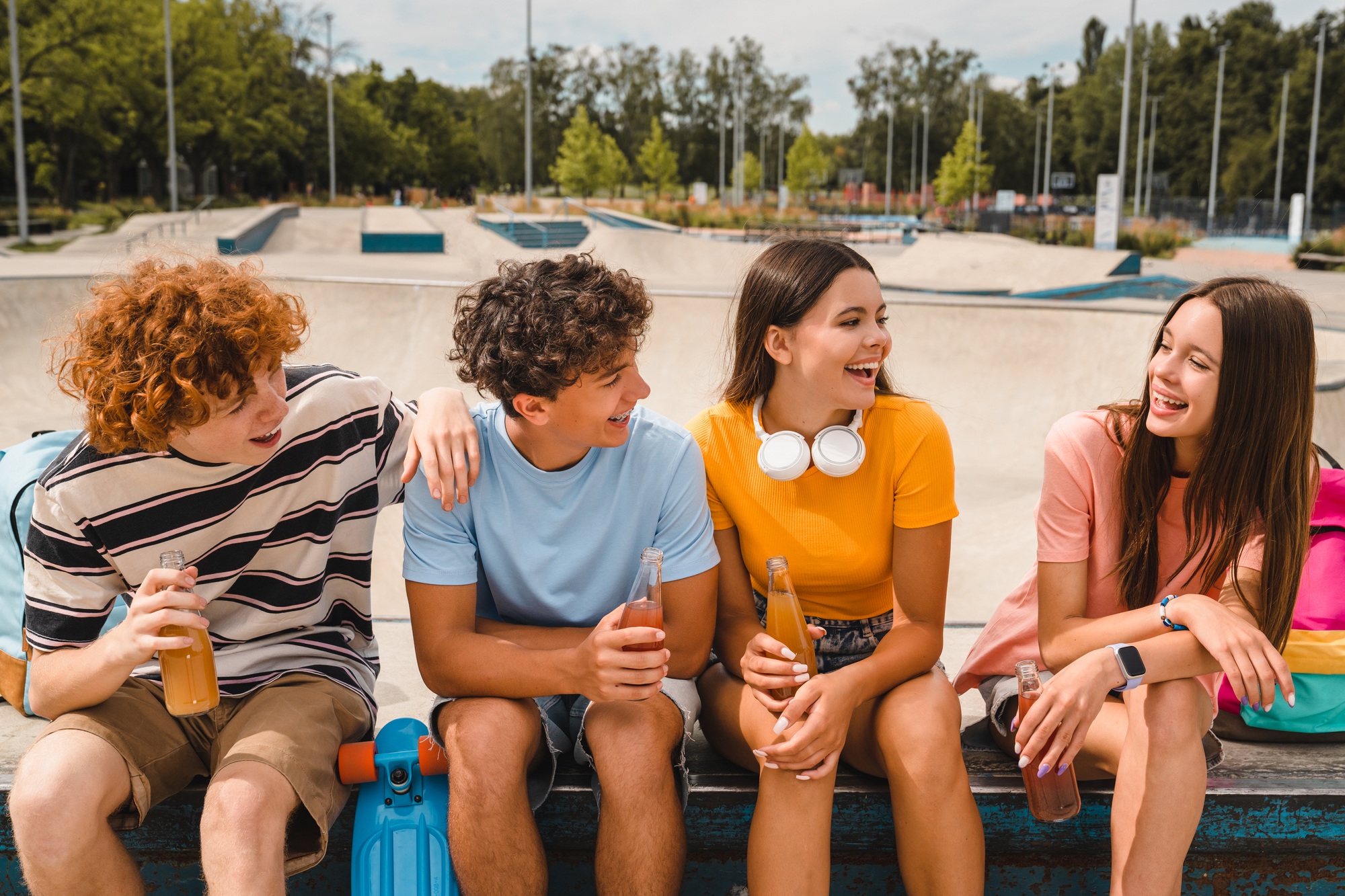 Smiling high school pupils sitting in skate park drinking soft dings lemonade hanging out outside